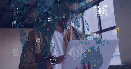 Data analyst wearing brown shirt working on laptop in workspace, with world map overlay