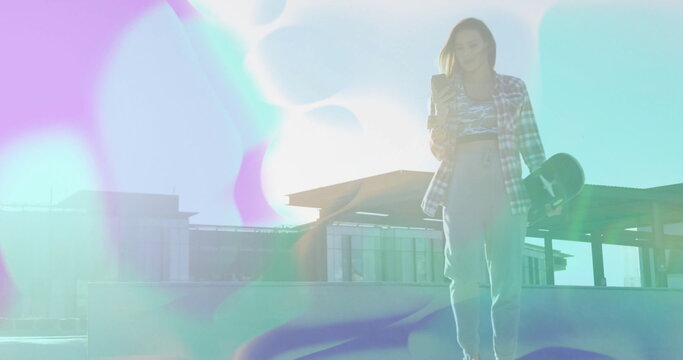 Holding skateboard and checking smartphone, woman skater in flannel shirt on rooftop, copy space - Powered by Adobe
