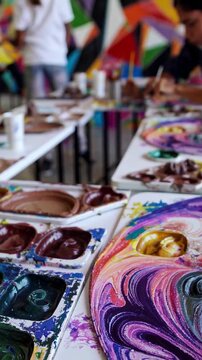 Elementary school students painting colorful artwork using acrylic pouring and swirling technique during art class in school, developing their creativity and artistic skills