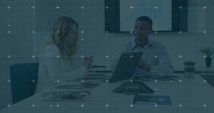 Reviewing charts, colleagues analyzing laptop screen in meeting room, with coffee cup and plant