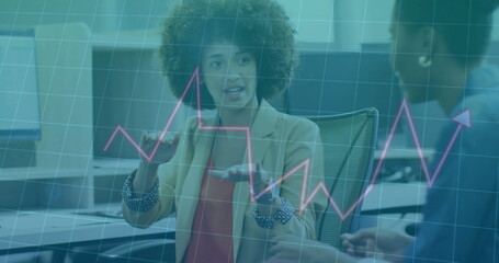 Gesturing woman in beige blazer and red blouse analyzing data, with overlaid line graph in office
