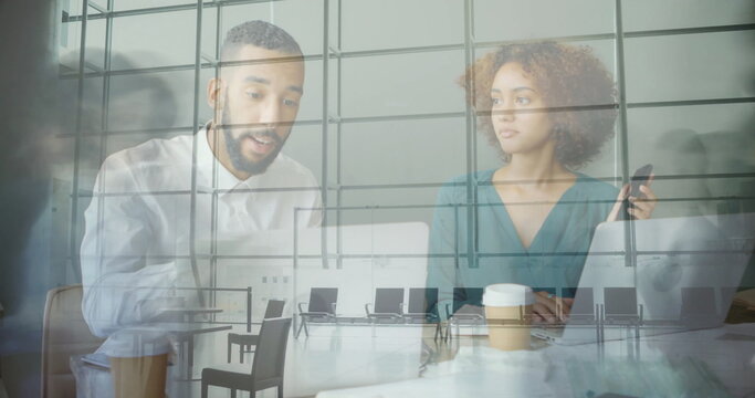 Two professionals collaborating at conference table, with laptops and grid reflection on glass wall