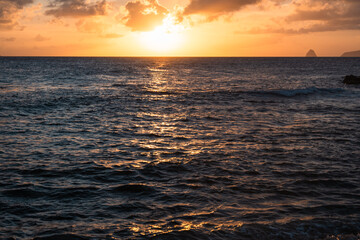 Golden Sunset Over Ocean with Reflective Waves and Distant Rocky Island Peak