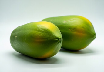 Two unripe green papayas with yellow spots on a light gray background