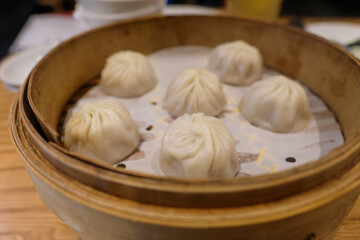 Traditional steamed dumplings served in a bamboo steamer basket at an Asian restaurant. Perfect for illustrating Asian cuisine, dining culture, restaurant menus, and culinary articles