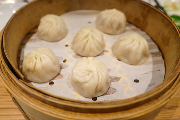 Traditional steamed dumplings served in a bamboo steamer basket at an Asian restaurant. Perfect for illustrating Asian cuisine, dining culture, restaurant menus, and culinary articles