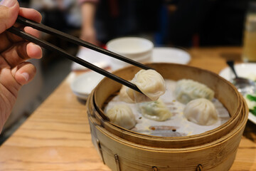 A traditional steamed dumplings being lifted with chopsticks from a bamboo steamer basket in an Asian restaurant. Suitable for Asian cuisine, dining culture menus, and culinary articles.