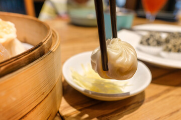 A traditional steamed dumplings being lifted with chopsticks from a bamboo steamer basket in an Asian restaurant. Suitable for Asian cuisine, dining culture menus, and culinary articles