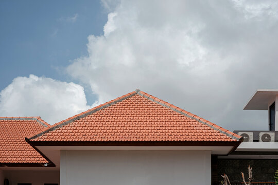 Architectural detail of a classic terracotta tile roof on a modern tropical house against a blue sky. Real estate and construction concept.