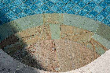 Curved stone steps leading into a refreshing blue mosaic tile swimming pool. An inviting top-down view perfect for summer vacation concepts.

