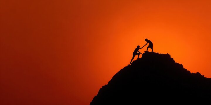 Two climbers work together on a steep slope during sunset, silhouetted against a vibrant orange sky. One climber reaches down to assist the other in their ascent.