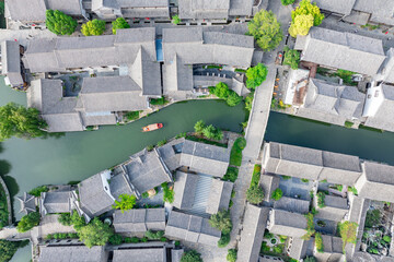 A boat travels down a serene waterway through the historic Taierzhuang Scenic Area in China, with traditional tiled roofs and bridges lining the banks.