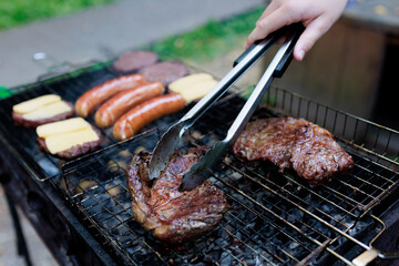 steaks are grilled and shot with selective focus, with hamburger patties and sausages being prepared in the background