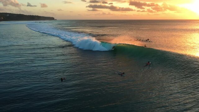 Drone video of a surfer at Bingin Beach, Bali, attempting a fun left-hander during golden sunset light. The wave lines up beautifully but the rider loses balance mid-ride, creating a cinematic moment.