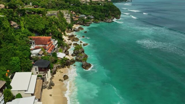 Drone footage flying along Bingin Beach shoreline in Bali, Indonesia, with a rising gimbal tilt that transitions from the beach to the cliffs while moving toward Impossibles surf break.