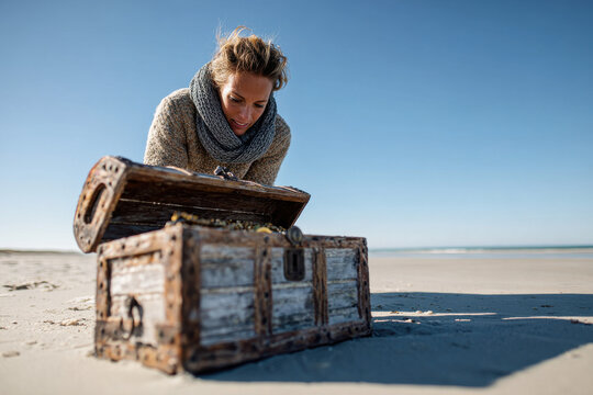 Woman looking inside treasure chest on deserted beach