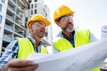 Engineer and builder reviewing architectural plans at construction site