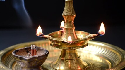 A traditional brass lamp and incense burner illuminate a dark backdrop with gentle smoke