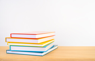 A stack of colourful books on a wooden shelf and white background