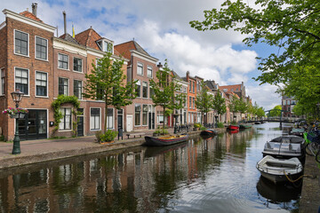 Historic gabled houses line a serene Leiden canal, reflecting vibrant Dutch charm under a bright sky. Perfect for showcasing European travel and traditional architecture.