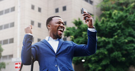 Success, businessman and celebration with phone in city for good news, commute and trading win. Trader, excited black person and victory fist in town for stocks growth, achievement or investment deal