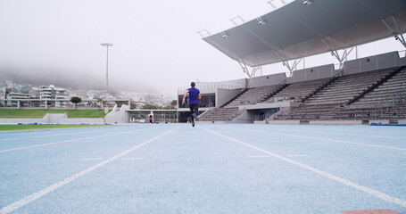 Running, athlete and back at stadium for sports competition, sprint or fitness practice. Training, speed and person outdoor as track runner, marathon and space for workout and wellness in low angle