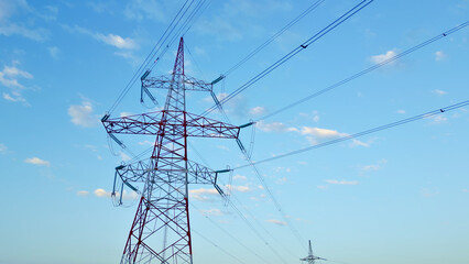 Hero perspective of powerful electricity pylons under a clear blue sky, symbolizing robust energy infrastructure. Steel structures support high-voltage power lines, essential.