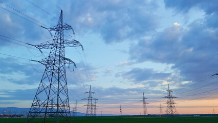 Power lines and pylons silhouette against a dusk sky in soft blue and pink, symbolizing sustainable...