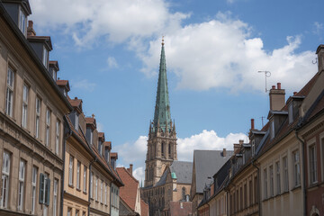 Fototapeta premium Tall green spire church between old European buildings under a cloudy sky architecture