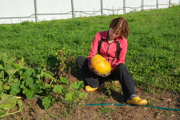 Mature woman in the garden holding yellow pumpkin in her hands, looking at it and smiling. Gardening and horticulture
