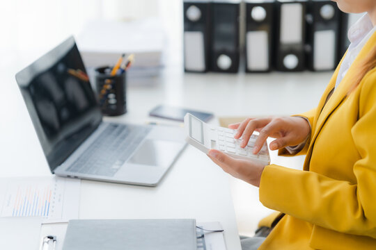 Financial Analysis: A professional meticulously calculates financial data with a calculator, using a laptop at her fingertips, documents and stationery filling the table.