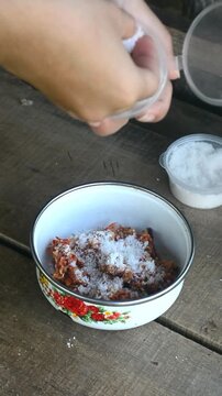 Close-up of hands preparing and marinating fish with herbs and spices for pepes ikan nila. Traditional cooking process.
