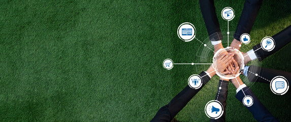 Aerial view of hands joining together on green grass, symbolizing collaboration and partnership in...
