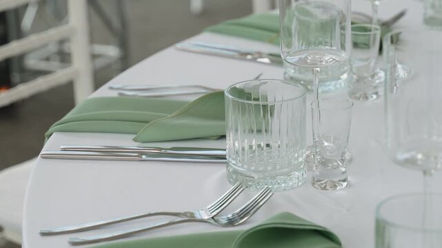 Clean prepared table set for banquet. Cutlery, various glasses and mint napkins are on round table on white tablecloth. Waiting for festive dinner.