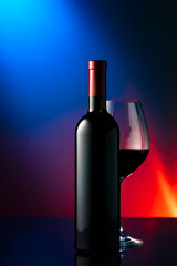 Glass and bottle of red wine on a black reflective background.