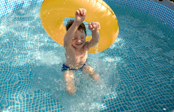Red-haired child playing with yellow swim ring in outdoor pool