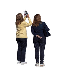 Deux femmes vues de dos en extérieur, leurs visages cachés par leurs cheveux, l’une en pull jaune prenant une photo avec son smartphone, l’autre en pull bleu marine portant un sac à main noir. 
