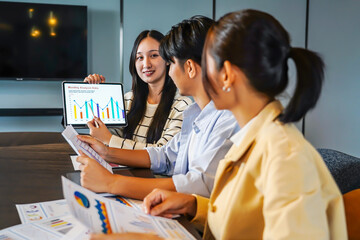 Group of asian motivated professionals engages in a strategic meeting, discussing business growth and online strategies. They use tablets and presentations to enhance collaboration and idea sharing.