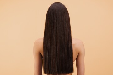 Woman showing her healthy, straight and shiny hair from behind on beige background.