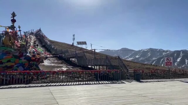 Snow-capped mountains with vibrant Tibetan prayer flags and wooden walkways in Amdo, Qinghai, highlighting Tibetan Buddhism culture in Greater Tibet.