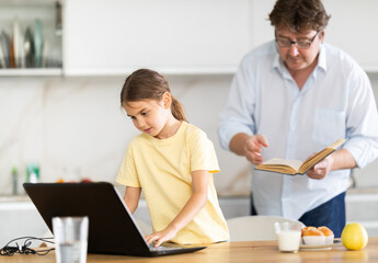 Obraz premium Father invites his little daughter to read an interesting book together. Daughter refuses and continues to play games on laptop