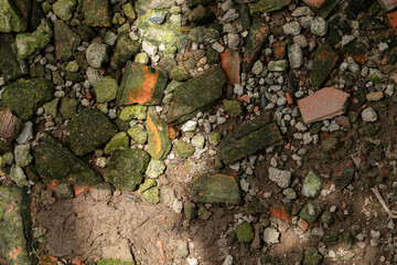 Grunge texture of broken terracotta tiles, stones, and moss on the ground. Abstract background of ruins and decay