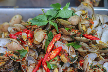Thai street food dish of stir-fried clams with basil and chili, served on a metal tray. Authentic seafood cuisine with rich spices and vibrant local flavors.