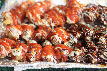 Thai teriyaki fried chicken with ketchup and mayonnaise, topped with sesame seeds on foil, vibrant street food fusion from Thai night market.