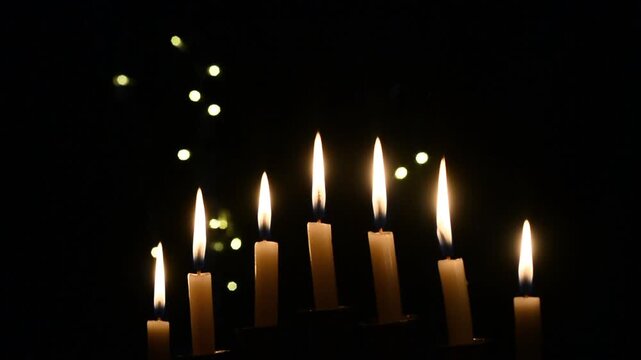 Hanukkah celebration candles glowing on a black background with warm festive light. Traditional Jewish holiday decoration featuring menorah candle flames, spiritual atmosphere, cultural symbolism, and