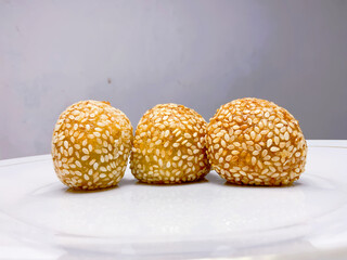 The traditional Indonesian food called onde onde sprinkled with sesame has a golden color and a round shape while placed on a white plate with a plain background