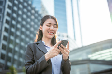 Asian young businesswoman using smartphone while standing in the city. 