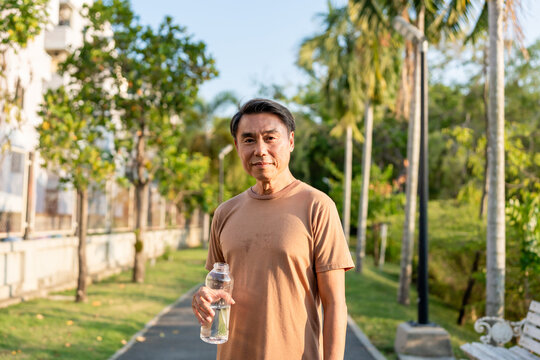 Portrait of Asian elderly man drinking water while running in garden. - Powered by Adobe