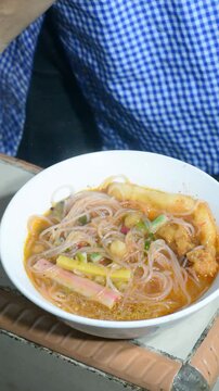 Homemade seblak cooking process with various toppings in a home kitchen. Popular Indonesian spicy street food prepared with authentic ingredients, flavorful seasonings, noodles, crackers, and assorted