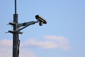 An Outdoor CCTV Security Camera On A Metal Pole Against A Light Blue Sky With Clouds. Urban Surveillance And Safety With Copy Space.